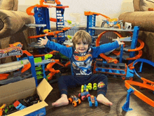 a young boy is sitting in front of a hot wheels track set