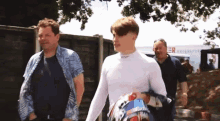 a man in a white shirt is carrying a helmet while walking with two other men