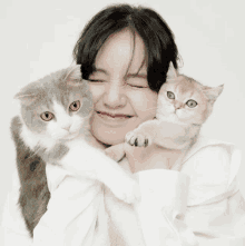 a woman in a white shirt holds two cats in her arms