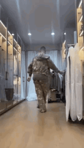 a man in a camo jacket is walking through a closet filled with clothes .