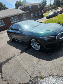 a green bmw is parked in a driveway in front of a brick building