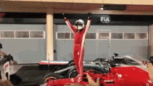 a man is standing on top of a red race car with his arms in the air in front of a fia sign