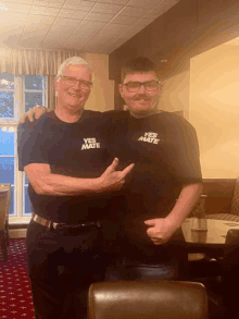 two men wearing shirts that say yes mate pose for a photo