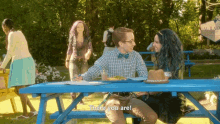 a man and a woman sit at a blue picnic table with the words " there you are " written on the table