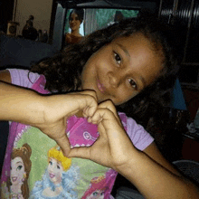 a young girl is making a heart with her hands .