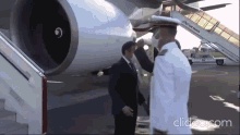 a man in a suit stands next to a man in a military uniform in front of an airplane that says air france