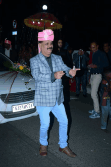 a man wearing a pink turban is standing in front of a white car with a license plate that says gj27ap709