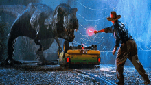 a man in a cowboy hat stands in front of a t-rex in a movie scene