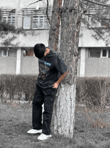 a young man leaning against a tree wearing a t-shirt that says " ed city radio "