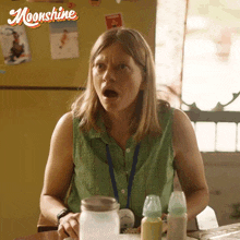 a woman is sitting at a table with a jar of milk and bottles in front of a refrigerator that says moonshine