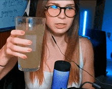 a woman wearing glasses is holding a glass of liquid in front of a sign that says #bestmod juggling pb 2