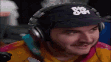 a man wearing headphones and a baseball cap is smiling while playing a video game .