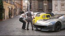 a man and a woman are standing next to a silver car with a license plate that says tf - 006