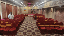 a man in a white shirt stands in a large room with red chairs