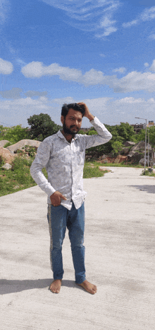 a man in a white shirt and blue jeans is standing on a concrete surface with his hand on his head