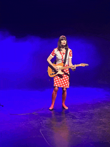 a woman in a red and white polka dot dress is holding a guitar on a stage