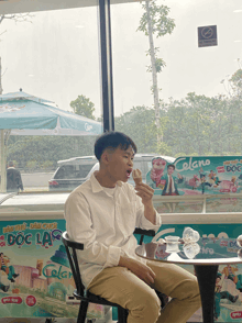 a man sits at a table eating an ice cream cone in front of an ice cream display that says celano