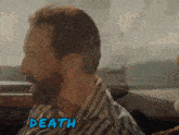 a man with a beard is sitting in a car with the word death written on his face