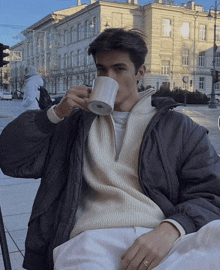 a man in a white sweater is drinking from a cup