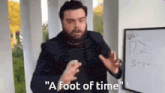 a man with a beard says " a foot of time " in front of a white board