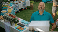 a man in a blue shirt is holding a box in front of a table that says run the barbeque