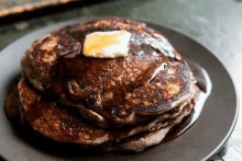 a close up of a stack of pancakes with syrup and butter on a black plate .