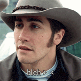 a close up of a man wearing a cowboy hat with bleh written below him
