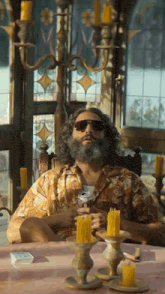 a man with a beard and sunglasses sits at a table with candles on it
