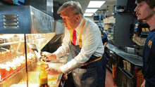 a man in an apron is pouring sauce on french fries in a mcdonald 's kitchen