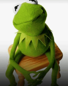 a kermit the frog sits on a wooden stool