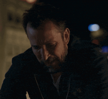 a man with a beard is wearing a black jacket with a logo on it