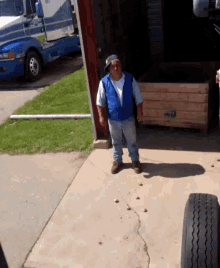 a man in a blue vest is standing on a sidewalk in front of a truck with a license plate that starts with the letter v