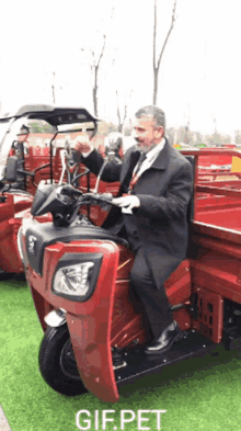 a man in a suit and tie is riding a red three wheeled vehicle with the word gifpet on the bottom