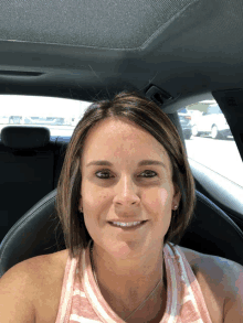 a woman in a pink and white striped tank top smiles while sitting in the back seat of a car