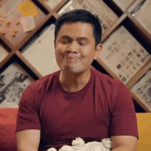 a man in a red t-shirt is sitting on a couch eating a cake .