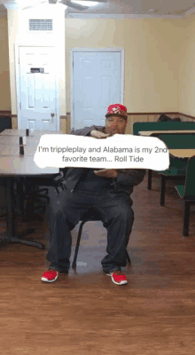 a man sits in a chair holding a sign that says i 'm tripleplay and alabama