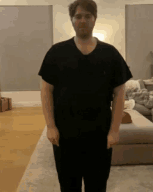 a man standing in a living room wearing a black polo shirt