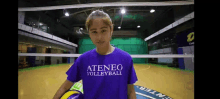 a woman wearing a purple ateneo volleyball shirt is holding a volleyball