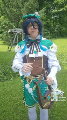 a man in a cosplay costume is holding a harp in a grassy field .