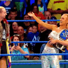 a man and a woman are standing in a wrestling ring . the woman is holding a championship belt .