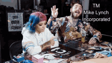 a man and a woman sit at a table with a sign that says " black lives matter " in the background