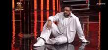 a man in a white suit and glasses is sitting on a stage .