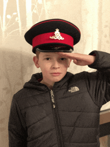 a young boy salutes while wearing a black jacket with the north face on it