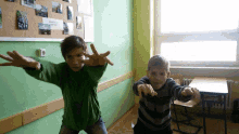 two boys are standing in front of a wall with pictures on it and one of them is wearing a green shirt and a striped shirt