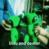 a person is holding two green stuffed aliens with the words lilou and dexter written on the bottom