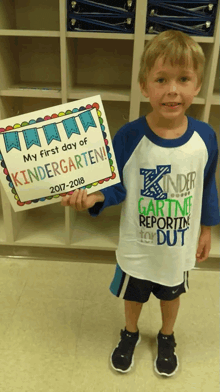 a young boy is holding up a sign that says my first day of kindergarten