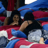 two women are laying on a bed and one is covering her mouth with her hand .