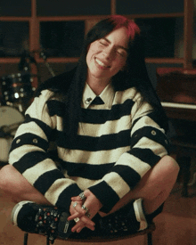 a woman wearing a striped sweater sits on a chair with her legs crossed