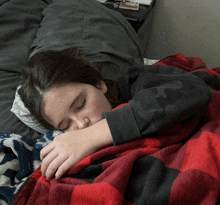 a girl is sleeping on a bed with a red and black plaid blanket