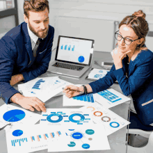 a man and a woman sit at a table looking at charts and graphs with the word marketing on the table